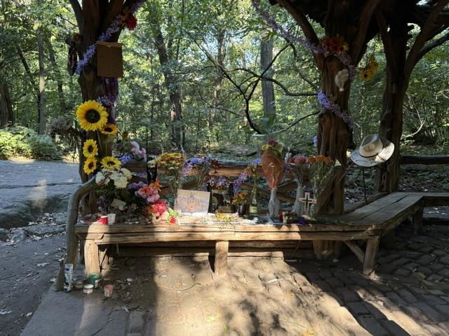Memorial for Lee in Central Park: a rustic bench covered with flowers, sunflowers, and her hat